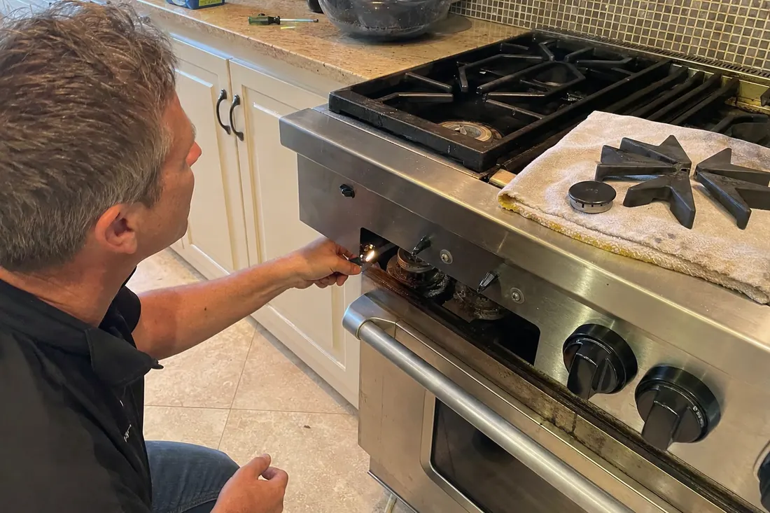 Technician checking the igniter on a dual-fuel range, one burner cap lifted off, the lifted grate in frame - Dacor repair in Jacksonville and Northeast Florida