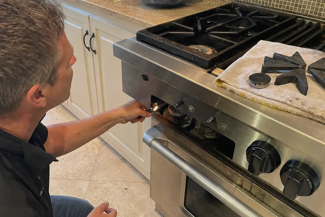 Technician checking the igniter on a dual-fuel range, one burner cap lifted off, the tile floor in frame - Wolf repair in Jacksonville and Northeast Florida