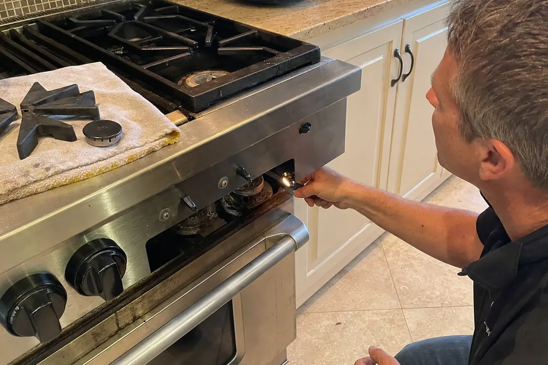 Technician checking the igniter on a dual-fuel range, one burner cap lifted off, the lifted grate visible in the picture - An Annual Maintenance Calendar for Built-In Appliances