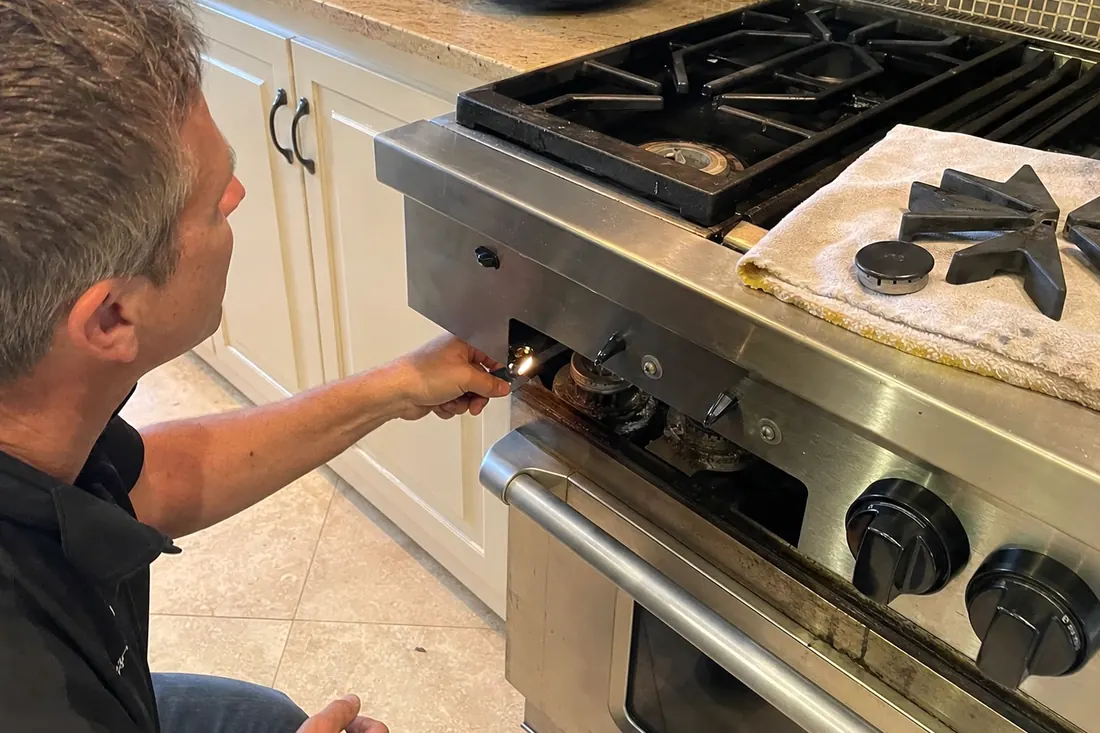Technician checking the igniter on a dual-fuel range, one burner cap lifted off, the exposed burner head visible in the picture - Troubleshooting