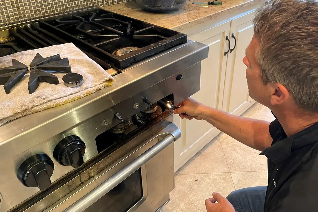 Technician checking the igniter on a dual-fuel range, one burner cap lifted off, the range front in frame - Outdoor Kitchen Appliance Repair