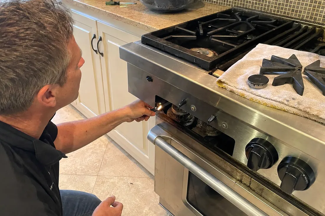 Technician checking the igniter on a dual-fuel range, one burner cap lifted off, the exposed burner head visible in the picture - What we guarantee, and what your manufacturer does