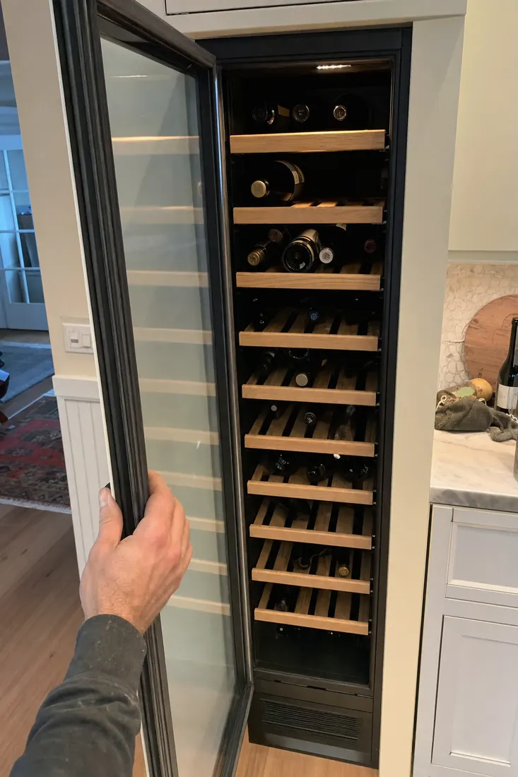 An open built-in wine column, bottles on wooden shelves, a hand at the door seal, the door gasket in frame - Perlick repair in Jacksonville and Northeast Florida