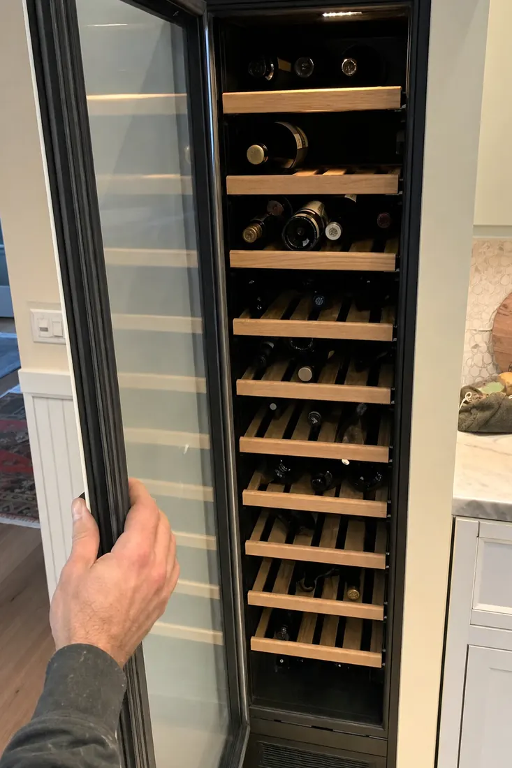 An open built-in wine column, bottles on wooden shelves, a hand at the door seal, bottles on their sides visible in the picture - What customers said afterwards