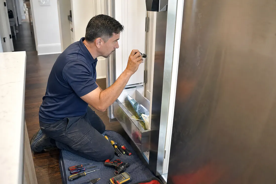 Technician checking inside an open built-in refrigerator with a flashlight, tools on a folded towel in frame - Scotsman repair in Jacksonville and Northeast Florida