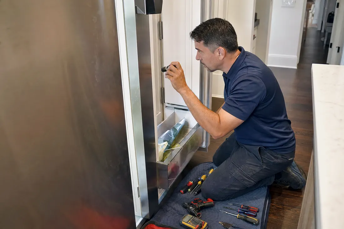 Technician checking inside an open built-in refrigerator with a flashlight, the glass shelves inside in frame - Sub-Zero repair in Jacksonville and Northeast Florida