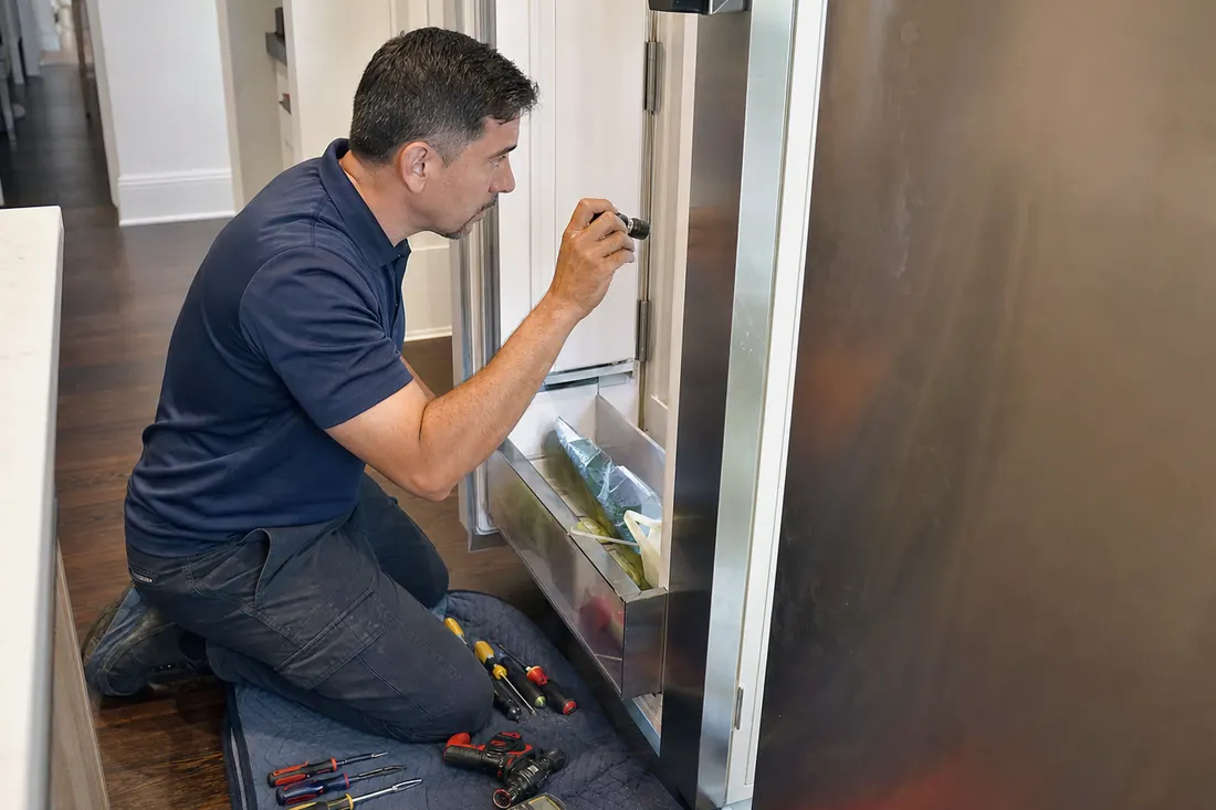 Technician checking inside an open built-in refrigerator with a flashlight, the open door visible in the picture - Built-In Ice Maker Not Making Ice