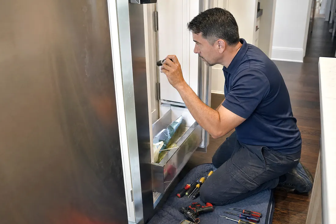 Technician checking inside an open built-in refrigerator with a flashlight, tools on a folded towel visible in the picture - Built-In Refrigerator Warm but the Freezer Is Fine?