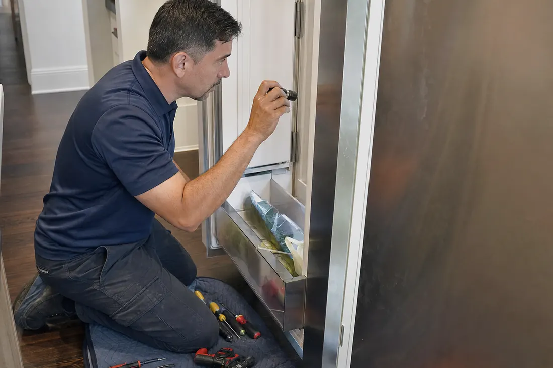 Technician checking inside an open built-in refrigerator with a flashlight - Getting a Built-In Out of Its Cabinet