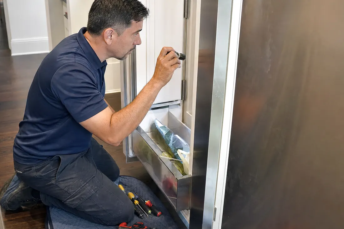 Technician checking inside an open built-in refrigerator with a flashlight, tools on a folded towel in frame - Panel-Ready Refrigerator Door Not Sealing Properly?