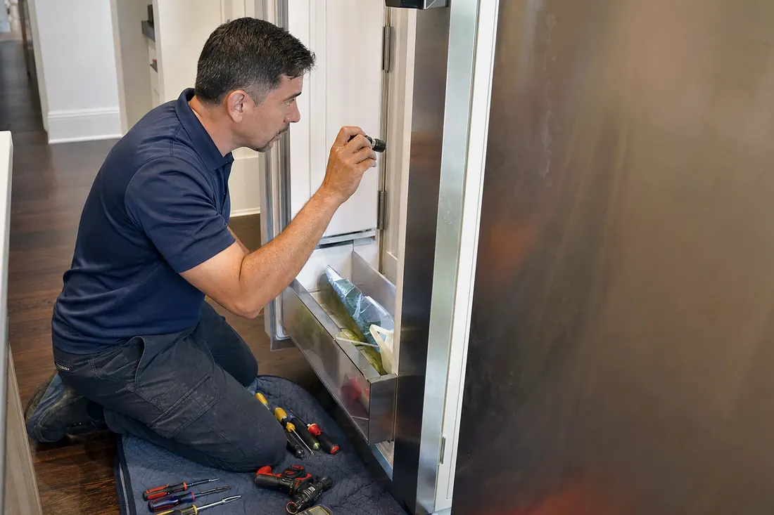 Technician checking inside an open built-in refrigerator with a flashlight, the glass shelves inside in frame - Sub-Zero and luxury appliance repair in Riverside