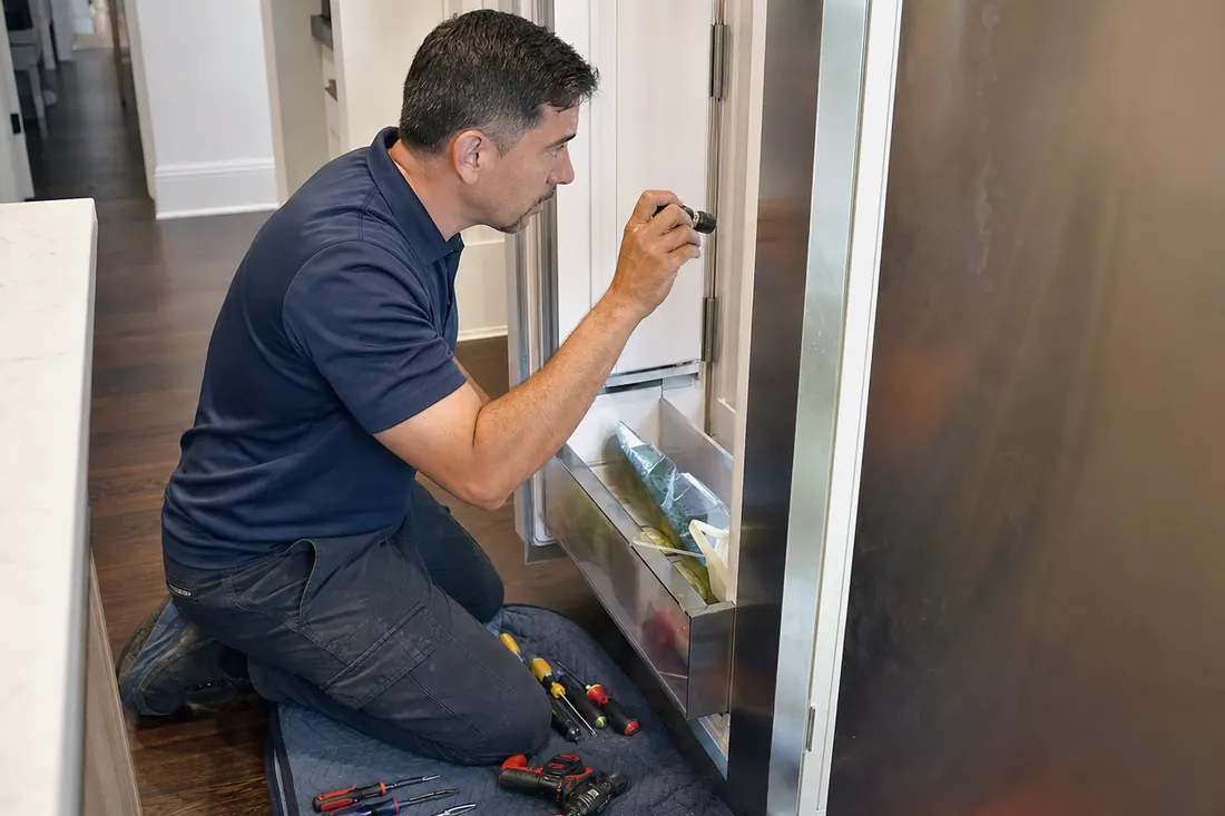 Technician checking inside an open built-in refrigerator with a flashlight, the open door visible in the picture - Freezer and Freezer Column Repair