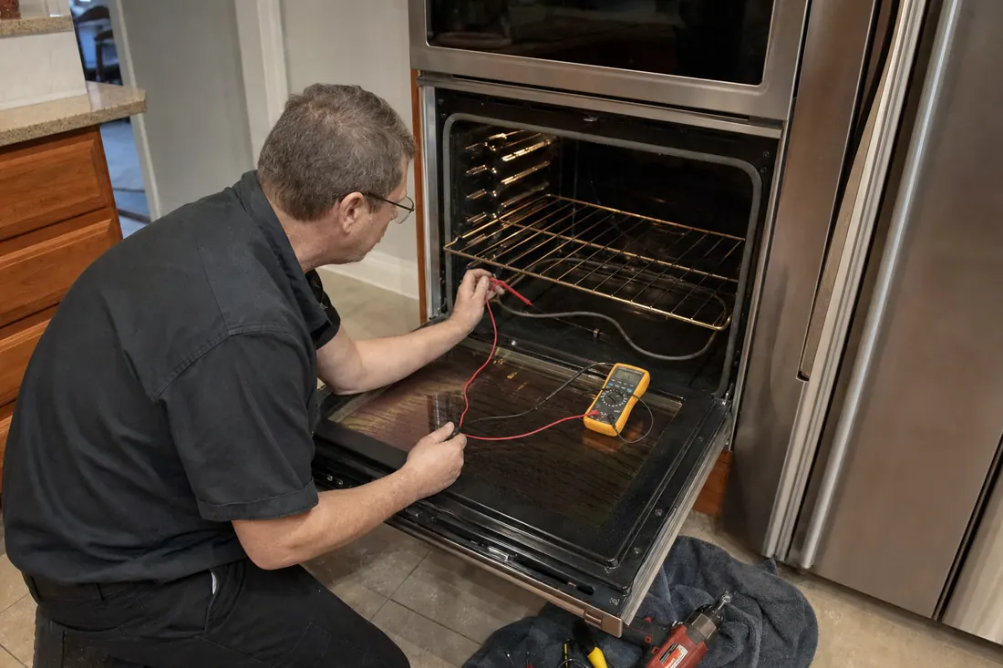 Technician testing the bake element of an open double wall oven with a multimeter, the oven racks in frame - Thermador repair in Jacksonville and Northeast Florida