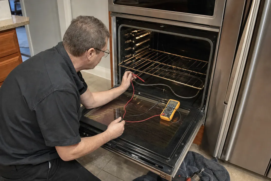 Technician testing the bake element of an open double wall oven with a multimeter, the multimeter leads visible in the picture - Installation